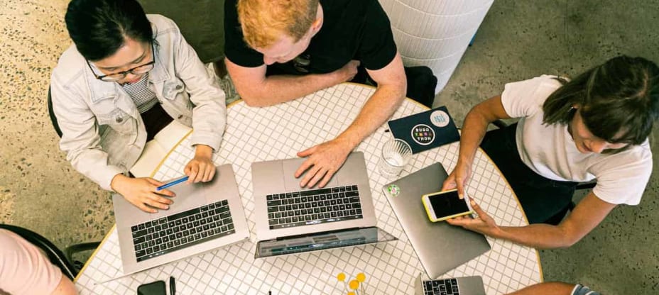 people sitting at a desk with laptops in front of them