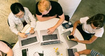 people sitting at a desk with laptops in front of them