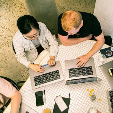 people sitting at a desk with laptops in front of them