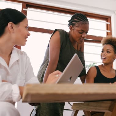 four women sitting by a desk in front of a computer, discussing