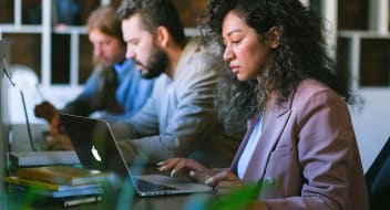 three people sitting at a desk in front of laptops