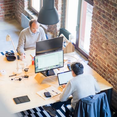 two men sitting in front of computers in an office space