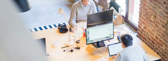 two men sitting in front of computers in an office space