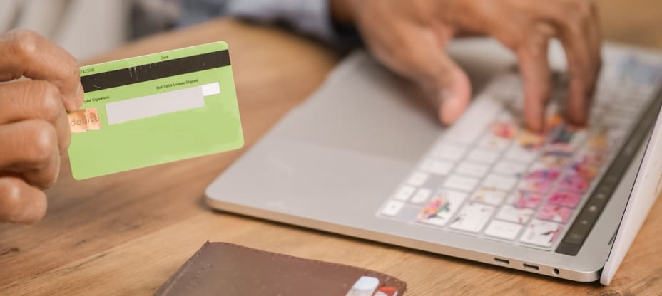 A hand holding a credit card and typing on laptop