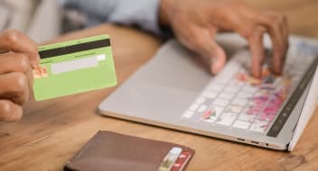 A hand holding a credit card and typing on laptop