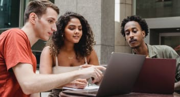 a group of people by a table, looking at a computer's screen