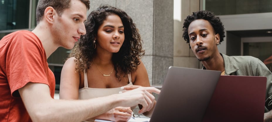 a group of people by a table, looking at a computer's screen