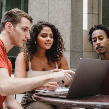 a group of people by a table, looking at a computer's screen