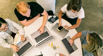 a group of people with macbooks sitting at a desk