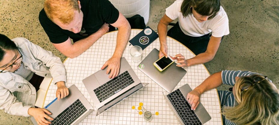 a group of people with macbooks sitting at a desk