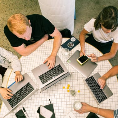 a group of people with macbooks sitting at a desk