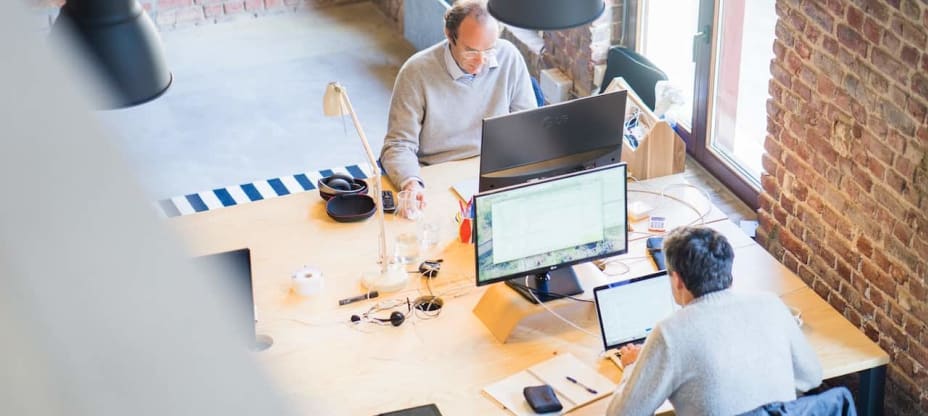 Two men sitting at a desk, working on laptops