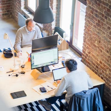 Two men sitting at a desk, working on laptops