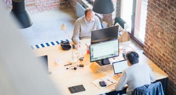 Two men sitting at a desk, working on laptops